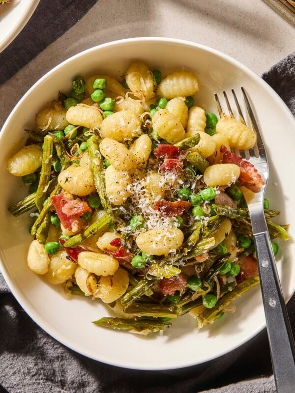 Bowl filled with gnocchi with bacon, asparagus, and peas.