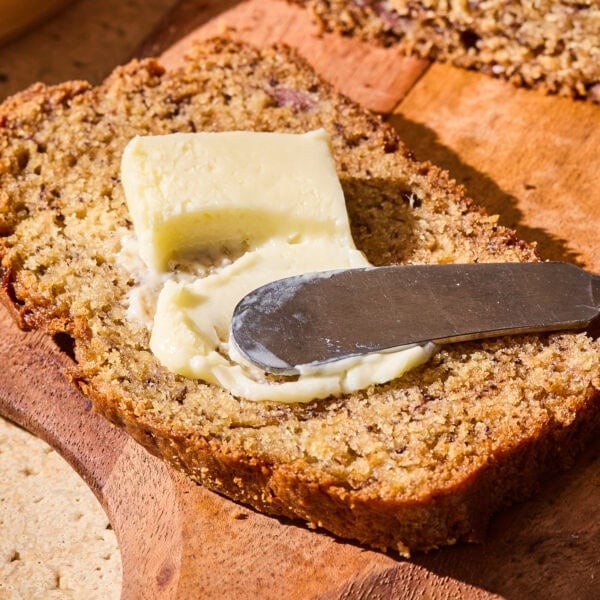 A pad of butter getting spread over a slice of banana bread.