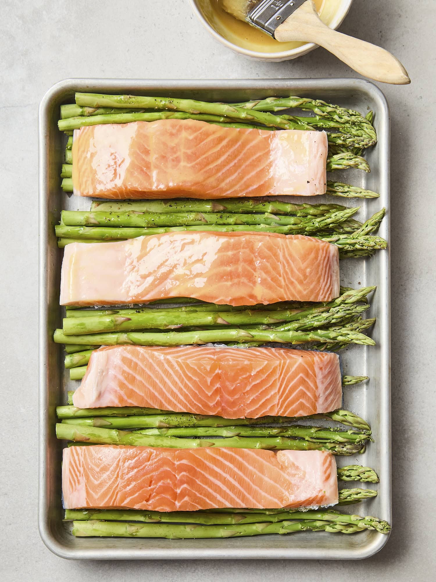 Uncooked fillets of salmon on top of asparagus on sheet pan.