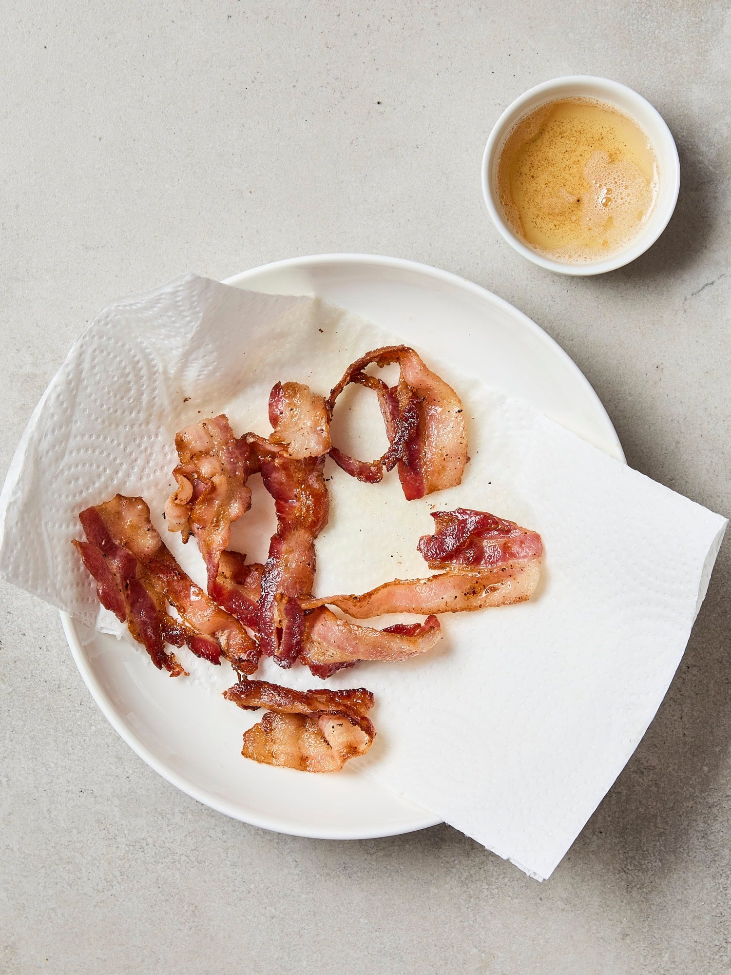 Cooked bacon on paper towel with bacon grease to side.