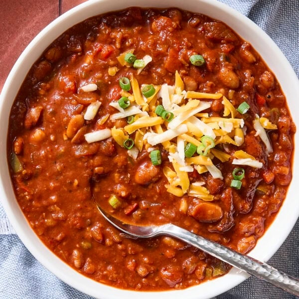 Bowl of chili with beans, cheese, scallions, and a spoon.