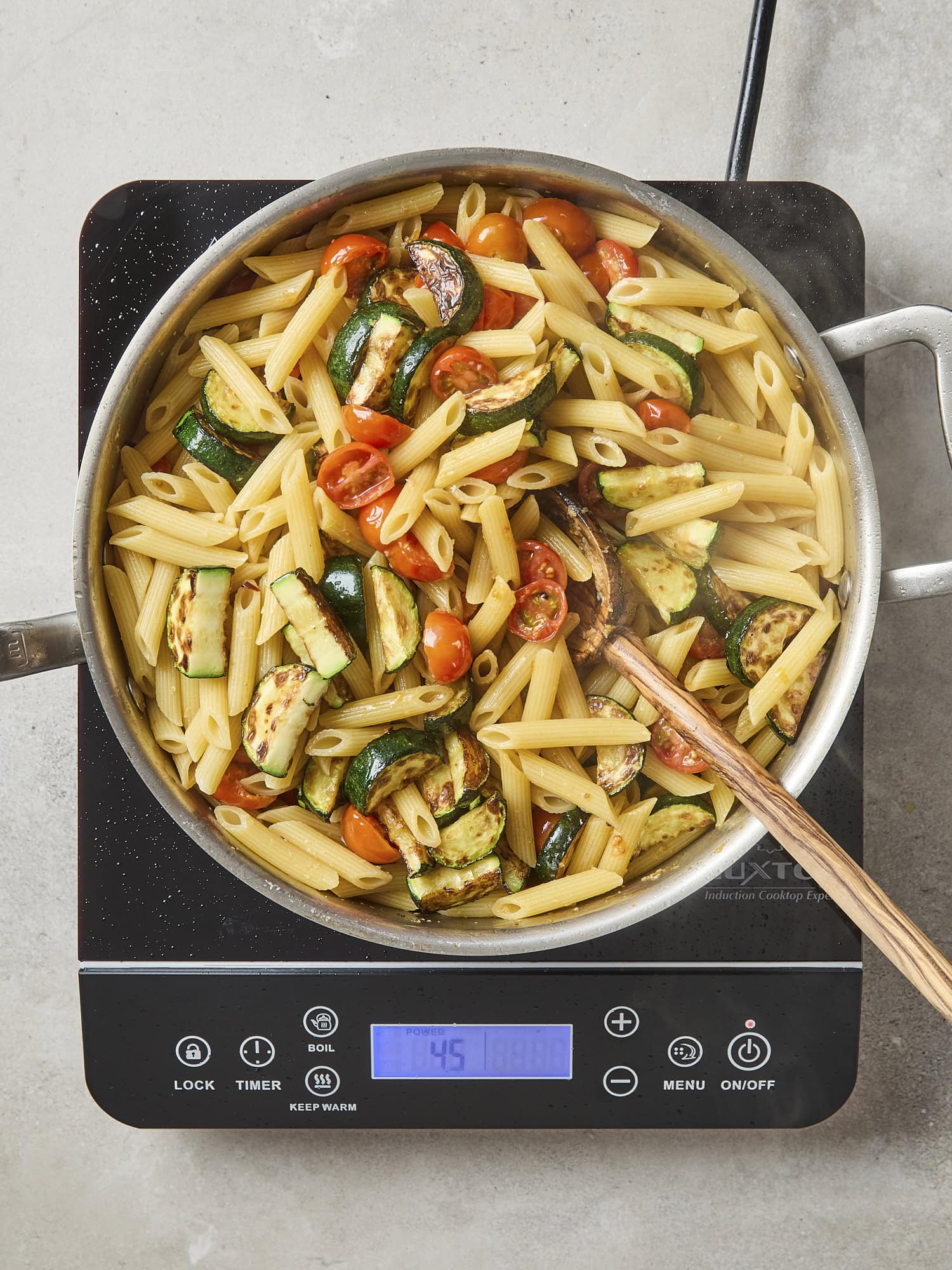Pasta being mixed with zucchini and tomatoes on heat.