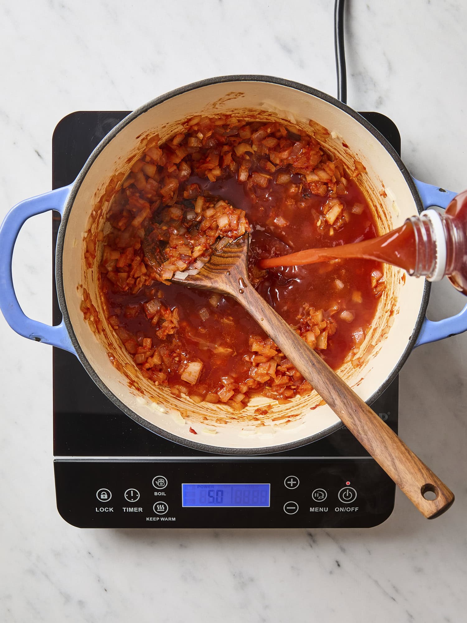 Tomato juice pouring into stockpot with cooked onions.