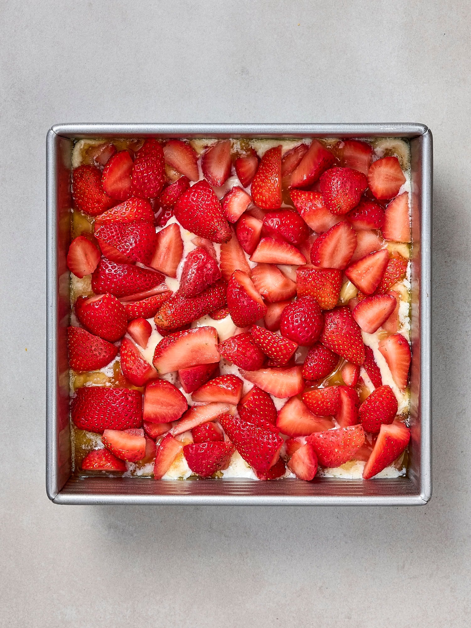 Strawberries sprinkled on top of batter in pan.