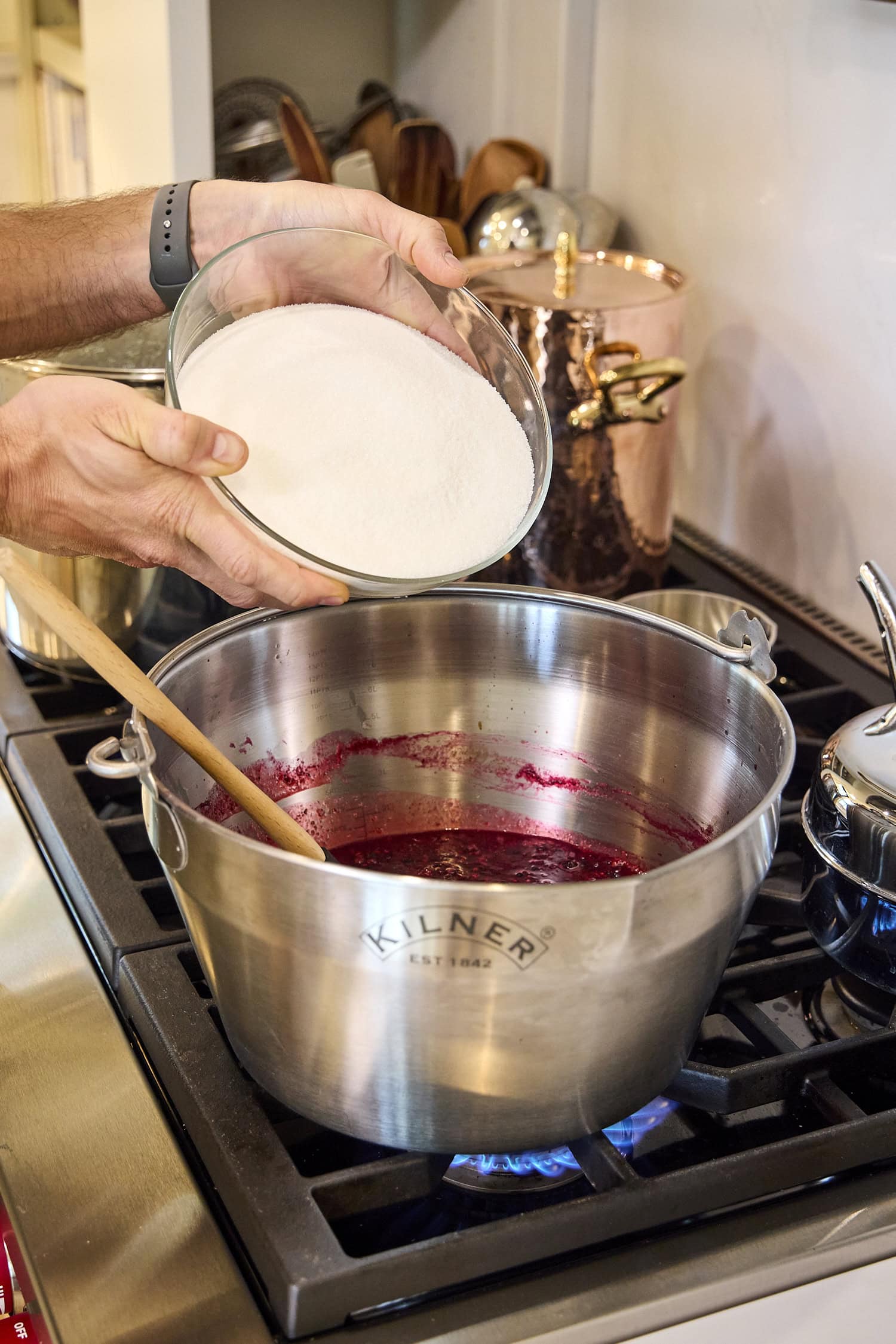 Pouring sugar into blackberry jam mixture on stove.