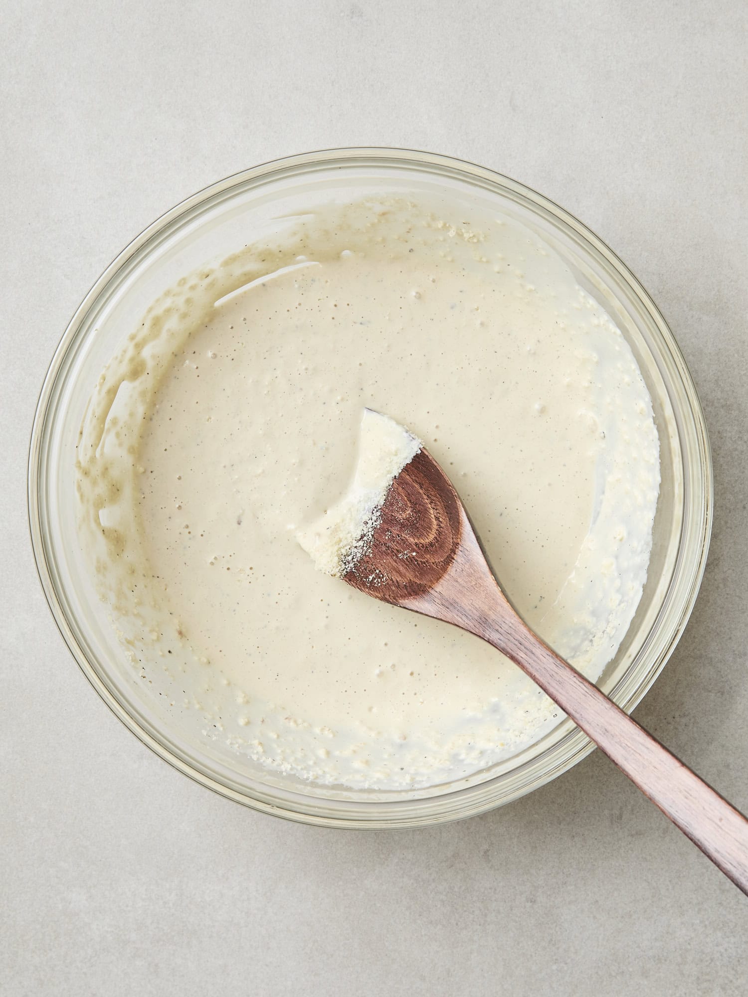 Glass bowl with mixed Caesar dressing with wooden spoon.