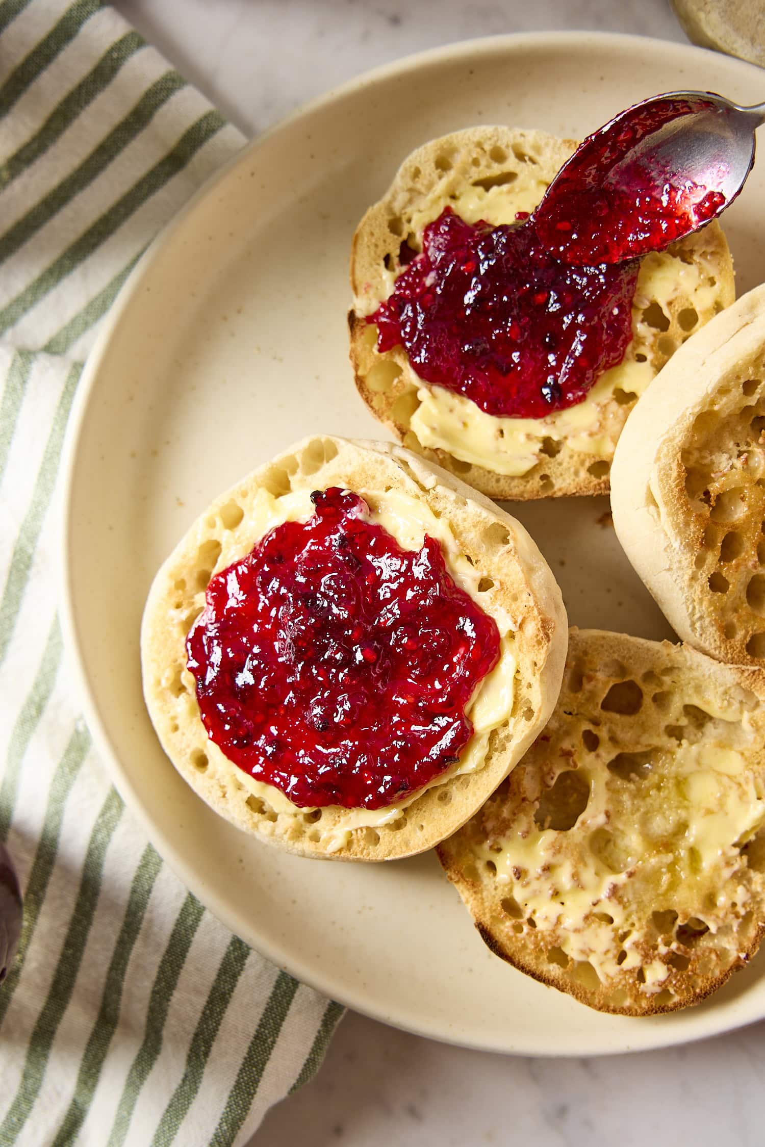 Muffins with butter and blackberry jam being spread.
