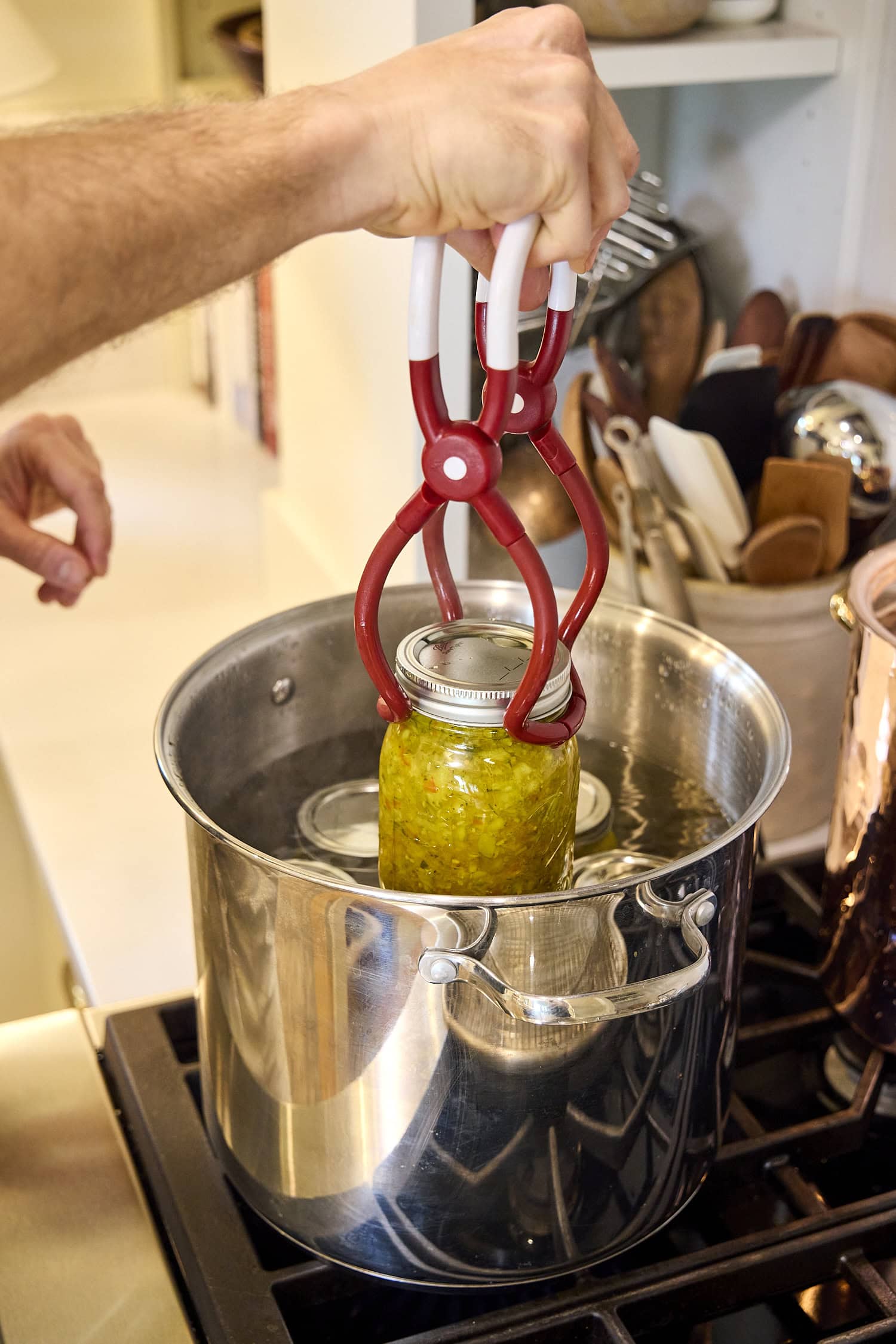 Adding glass canning jars filled with zucchini relish to waterbath canner.