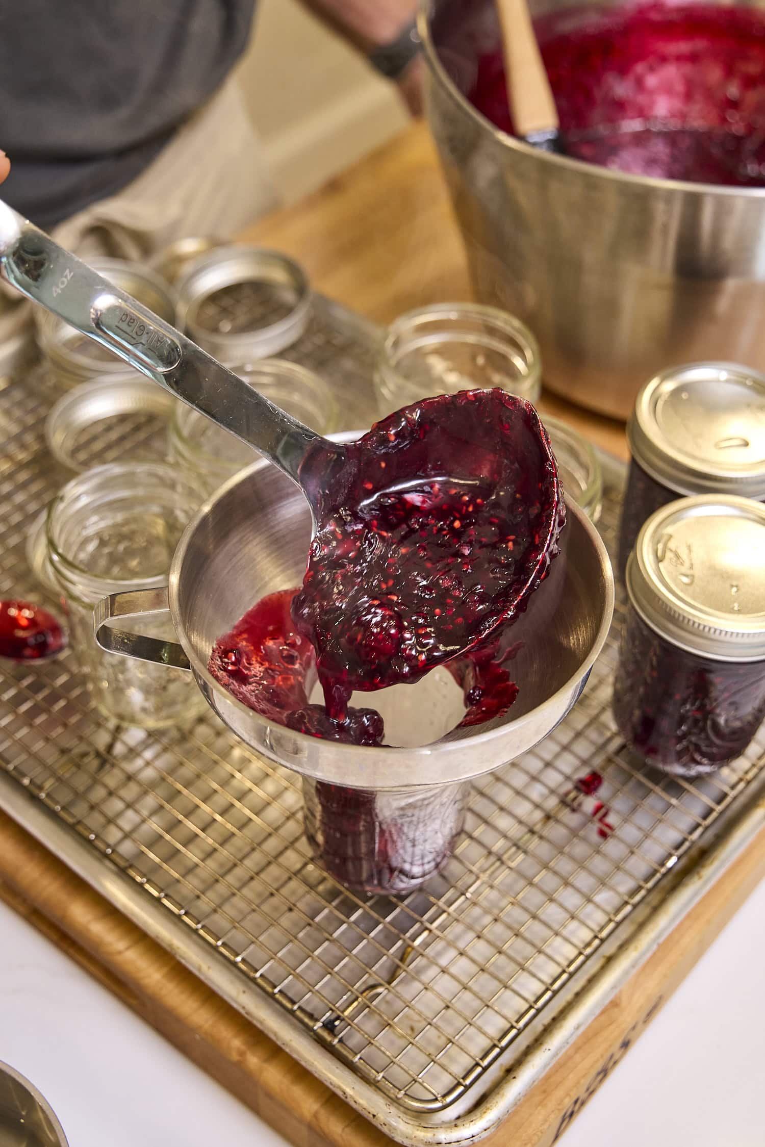 Using a ladle to put blackberry jam into jar.