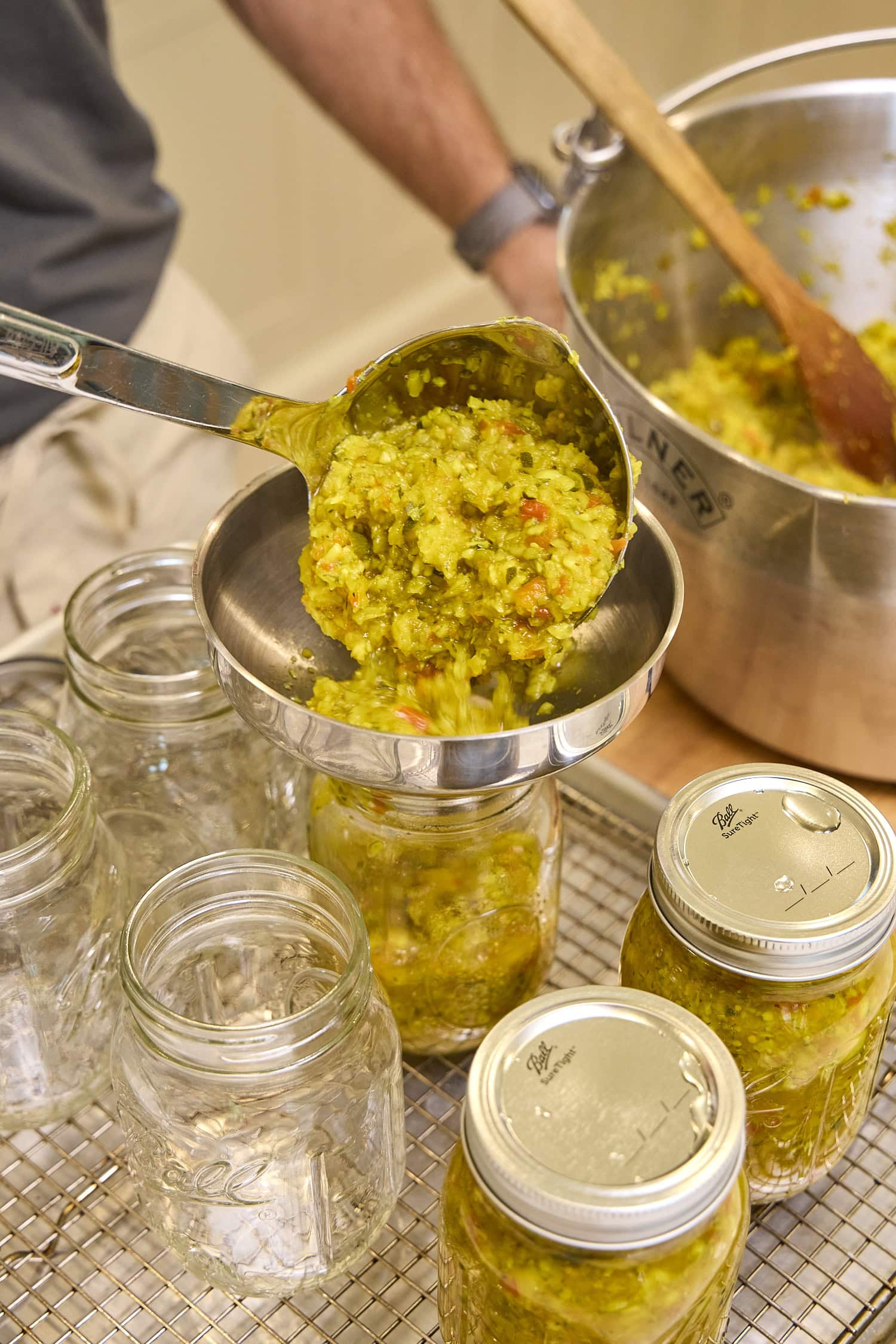 Lading zucchini relish into glass canning jar.