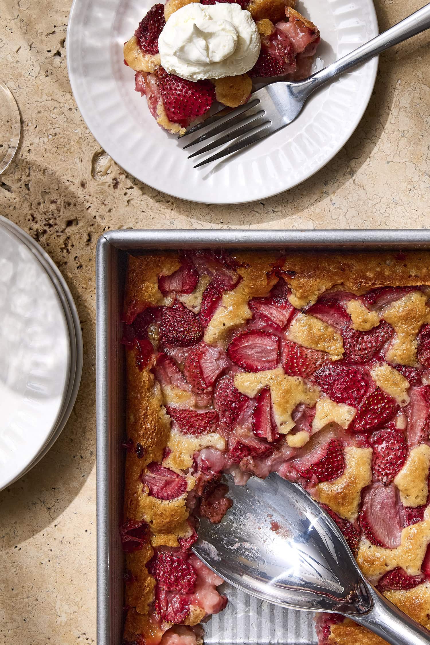Baking dish with strawberry cobbler with serving on plate with whipped cream.