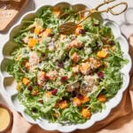 White bowl with butternut squash salad topped with cranberries, Parmesan, and walnuts.