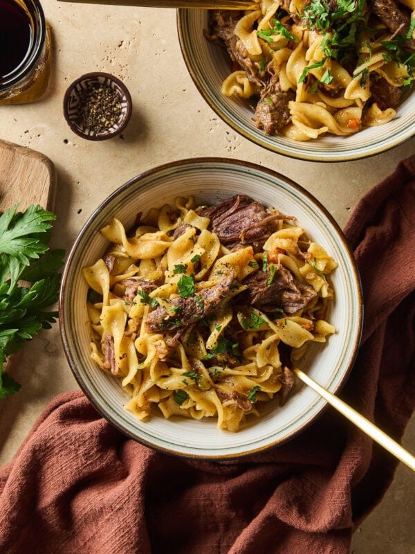 A bowl filled with beef and noodles rests on a table next to a napkin.