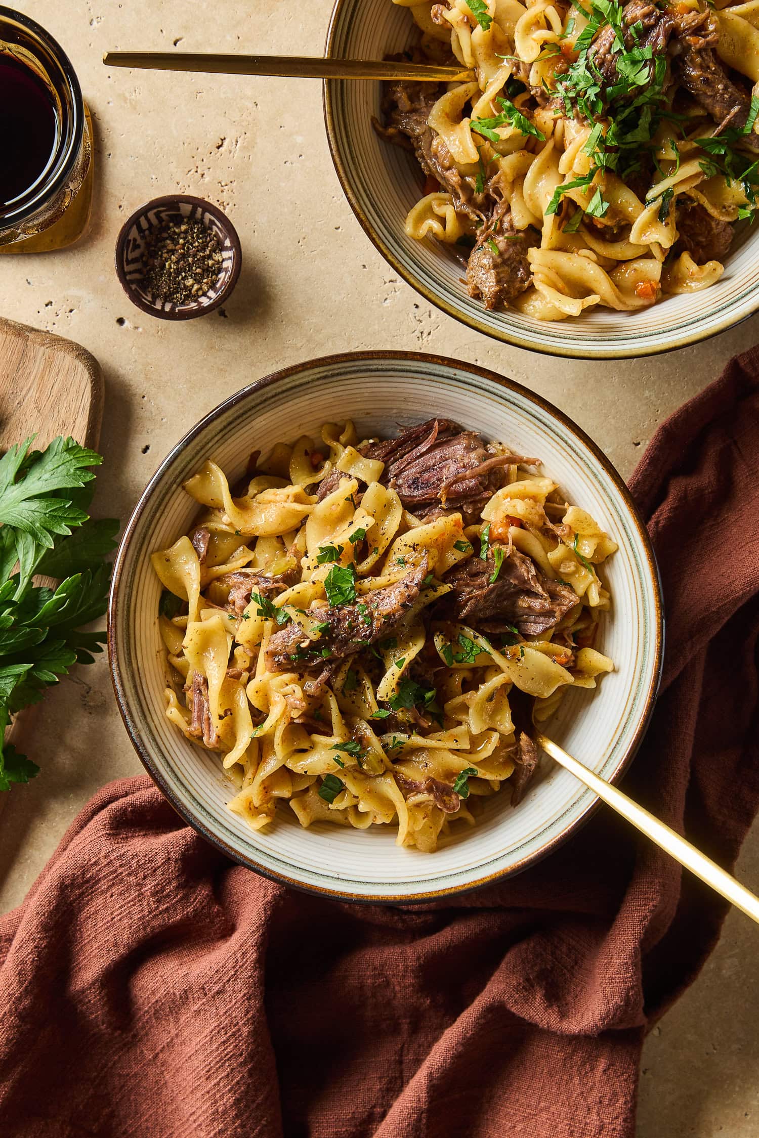 A bowl filled with beef and noodles rests on a table next to a napkin.