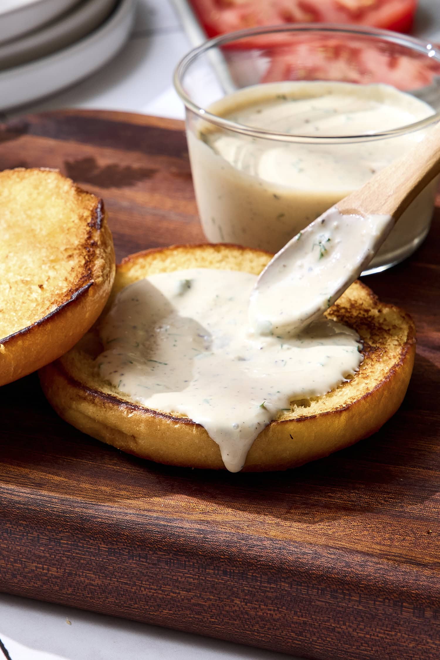 Spoon putting creamy herb sauce on a hamburger bun.