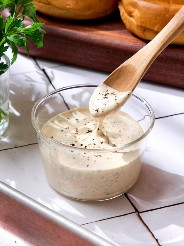 Glass bowl with spoon lifting creamy herb sauce.