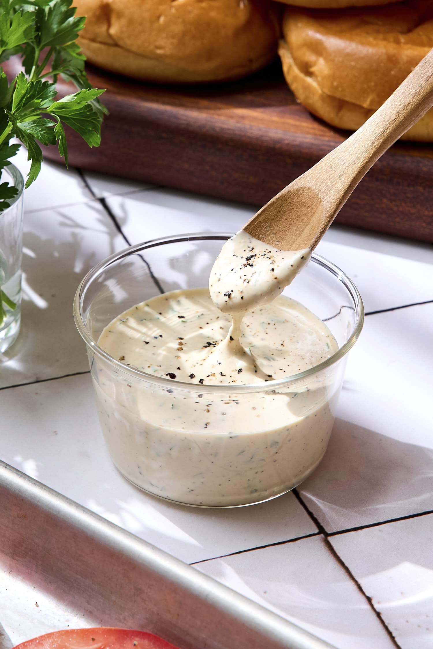 Glass bowl with spoon lifting creamy herb sauce.