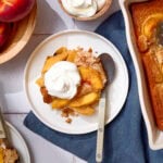 Easy peach cobbler served on a white plate with whipped cream.