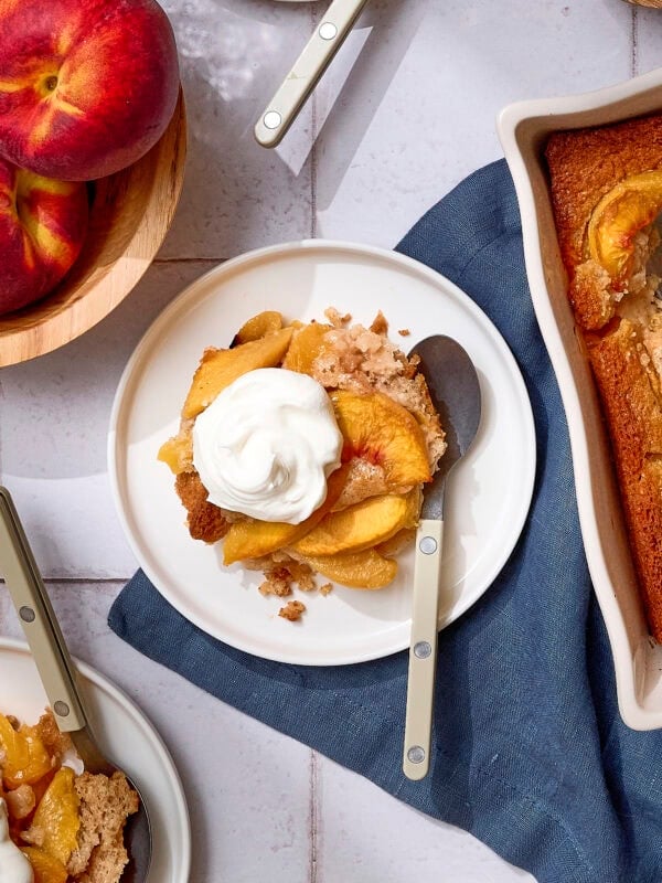 Baked peach cobbler on a plate with whipped cream on top.