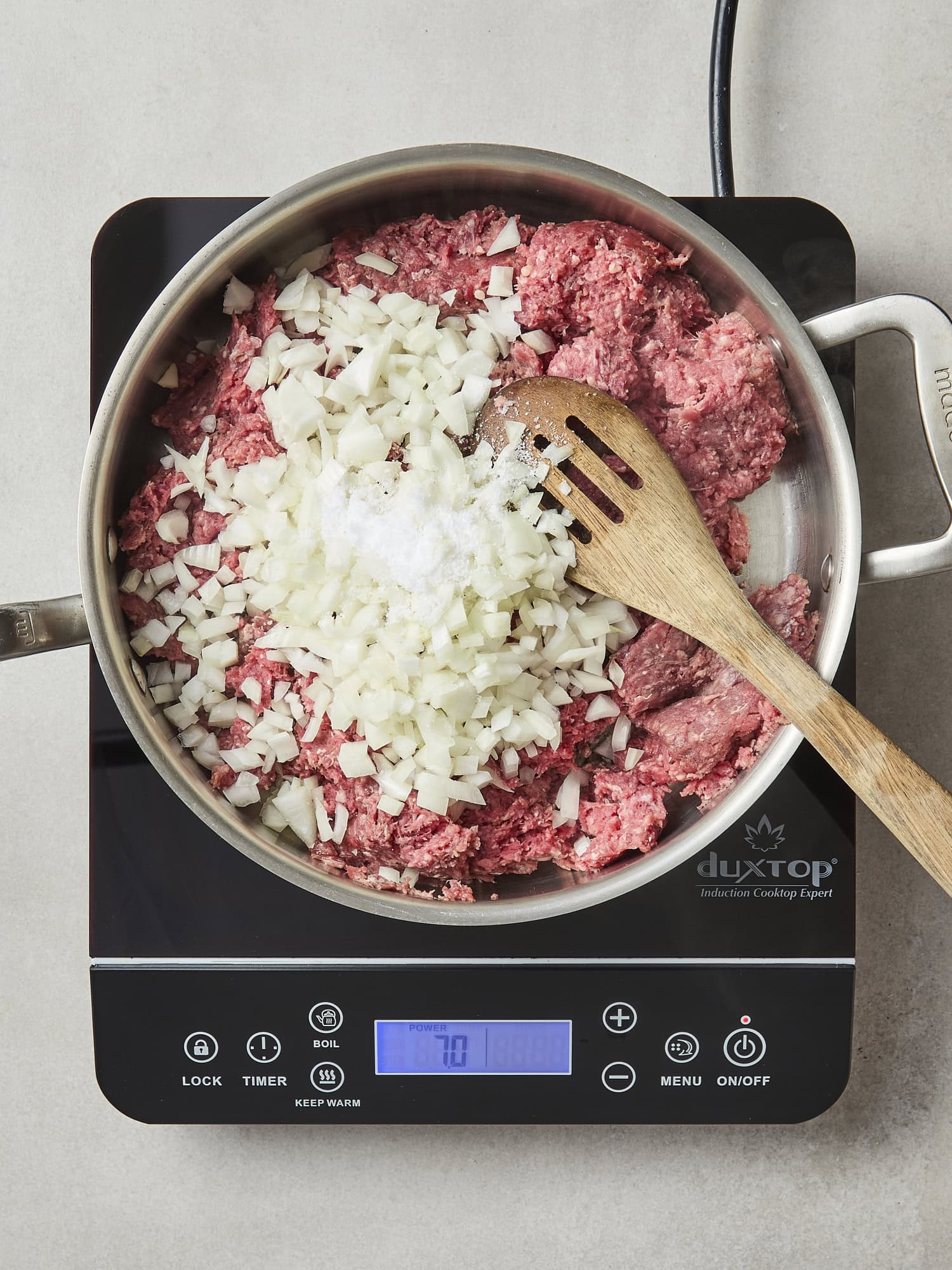 Raw ground beef and diced onion in a pan before cooking.