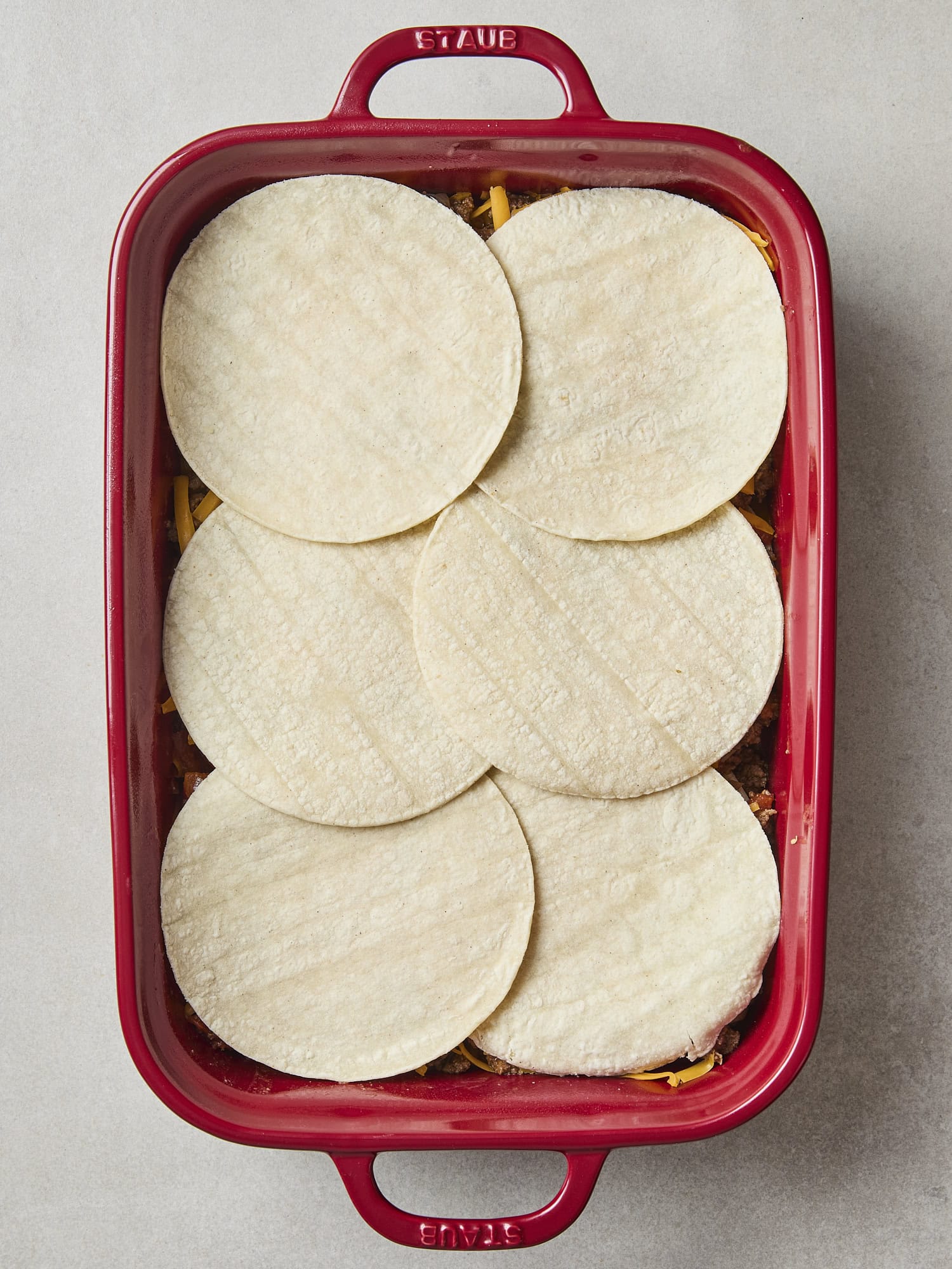 Corn tortillas layered on top of beef in casserole dish.