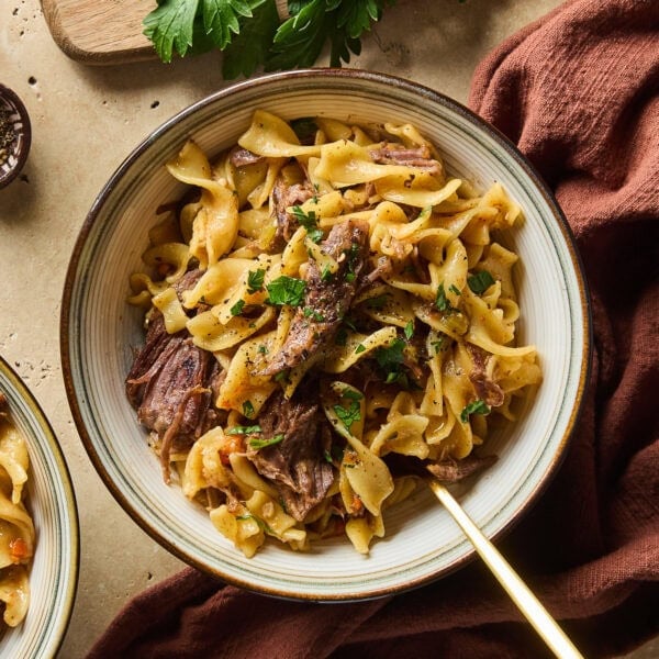 Two bowls of beef and noodles rest near a napkin on a tabletop.
