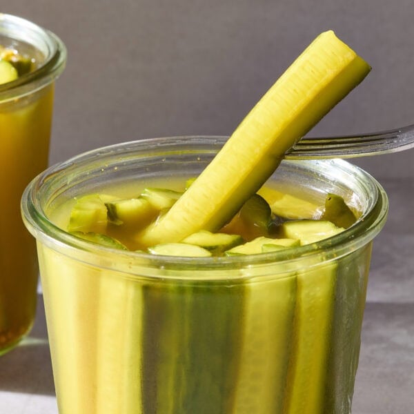 A fork pulling a speared pickle out of a jar.