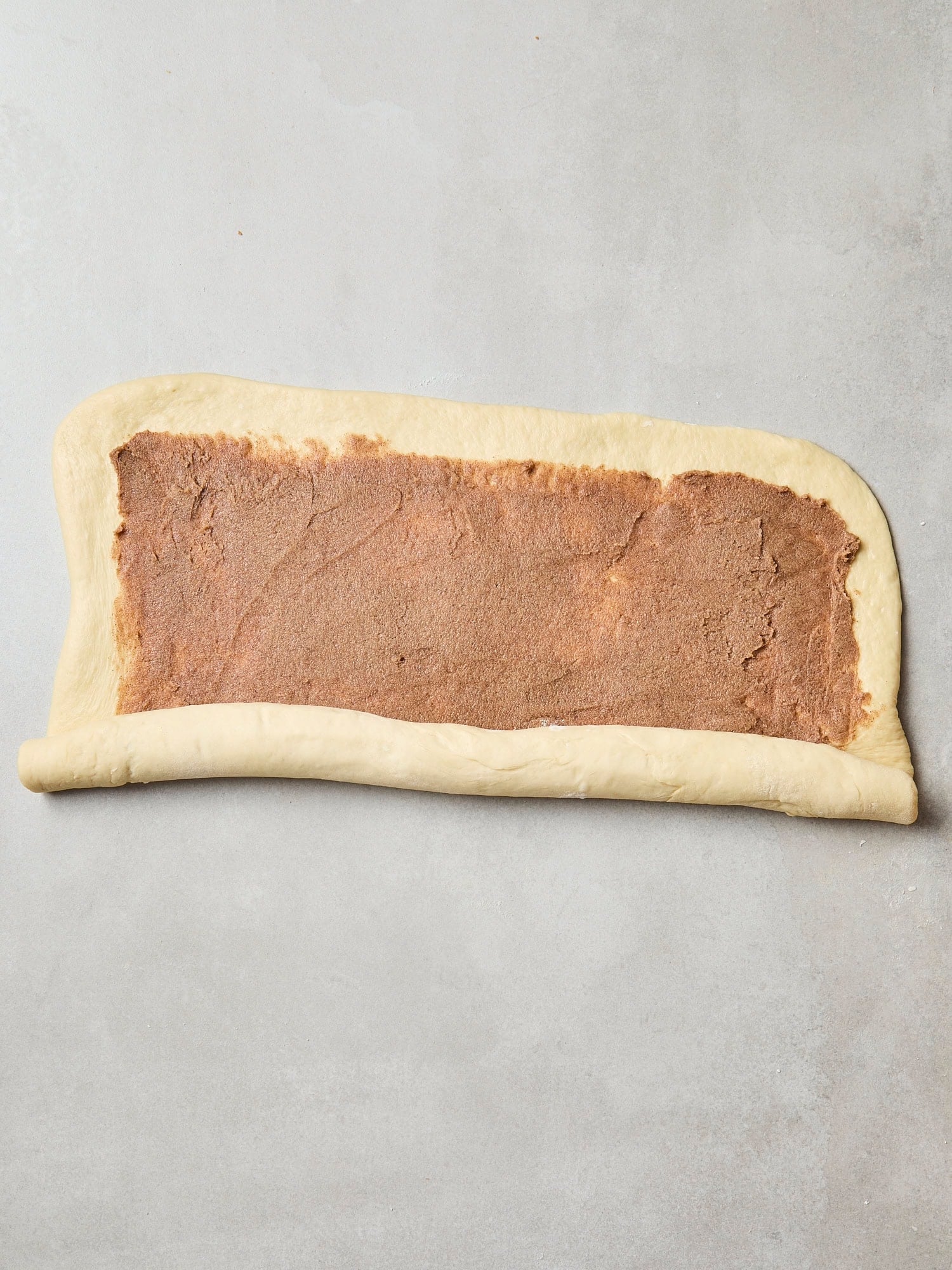 Cinnamon roll dough being rolled up into a log.
