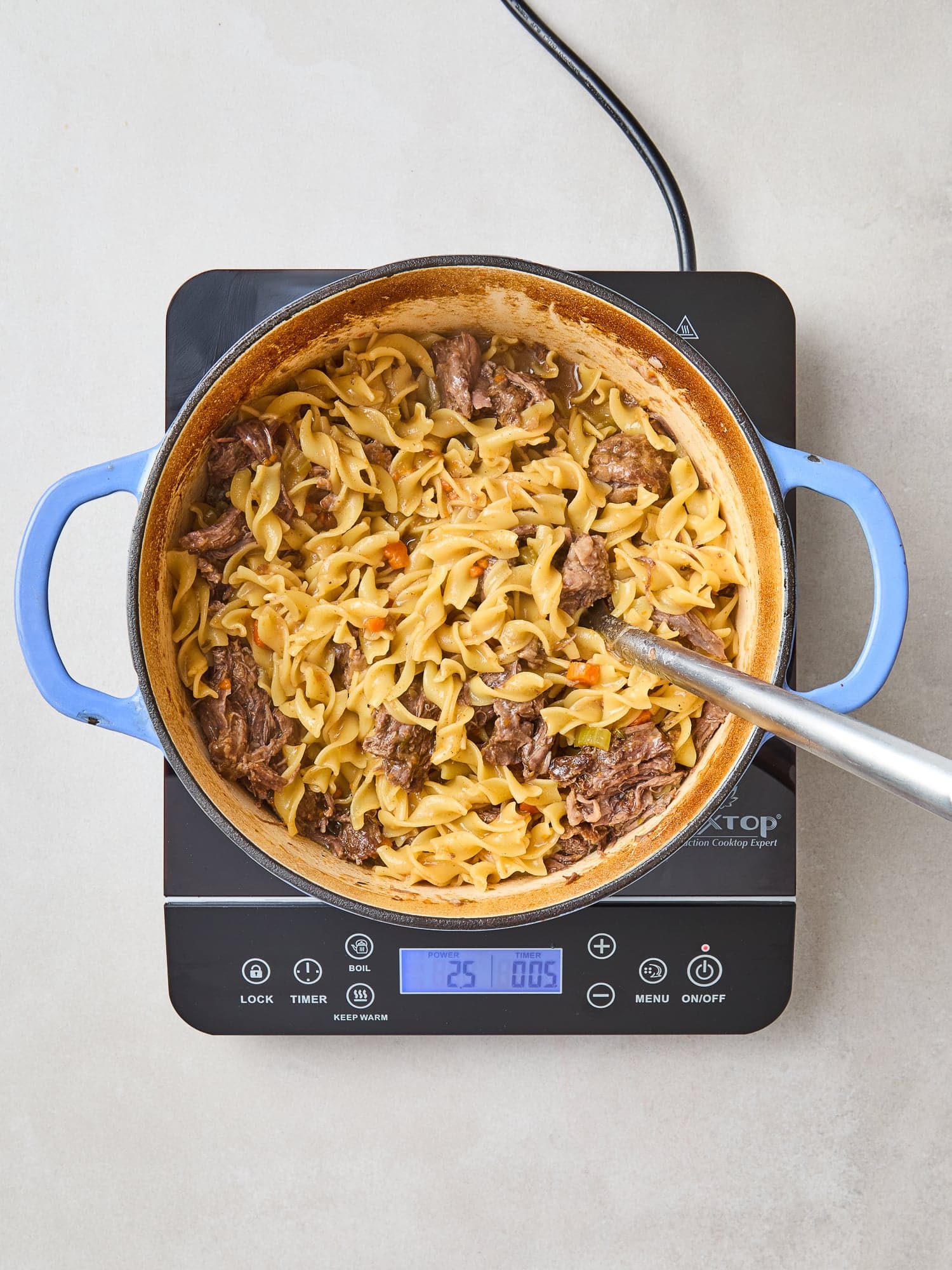 Shredded beef added into a pot with noodles.