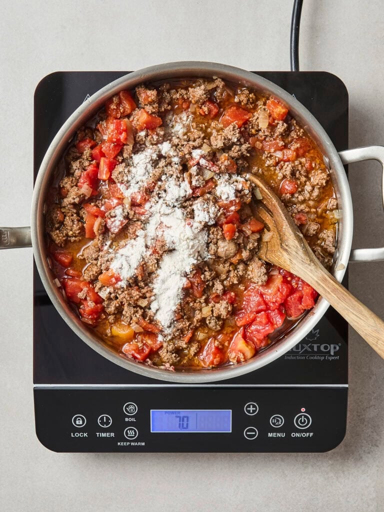 Adding flour to beef mixture on stove.